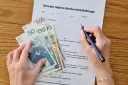 Umowa najmu i pieniądze na stole. Zastanawiasz się, jak zapłacić podatek od wynajmu mieszkania? Dokument i gotówka sugerują, że to czas na rozliczenie.