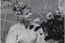 Ilona Stawińska w kwiecistej fryzurze i jasnej sukni, otoczona kwiatami, wygląda jak z baśni.
