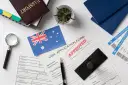 Paszport, formularz wizowy z pieczątką "APPROVED", flaga Australii, bilety lotnicze.