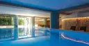 Indoor swimming pool with lounge chairs and a stone wall with warm lighting.