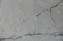 Popękany beton, jakby po długim okresie podlewania, z widocznymi szczelinami i drobnymi źdźbłami trawy.