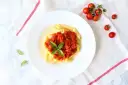 Penne z sosem pomidorowym i bazylią, obok świeże pomidorki koktajlowe.