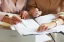 Dwie osoby analizują dokumenty, jedna wskazuje palcem na papier.