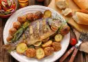 Pieczona ryba z ziemniakami, cytryną i rozmarynem na talerzu.