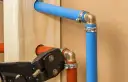Narzędzie do zaciskania rur pokazuje, jak łączyć rury plastikowe do wody, tworząc instalację z niebieskich i pomarańczowych rur.