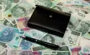Czarny portfel i długopis leżą na stosie polskich banknotów.
