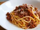 Pyszne spaghetti bolognese z bogatym sosem mięsnym i startym parmezanem na białym talerzu.