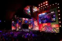 Kolorowa scena festiwalu Poland Rock 2026 z wielkim ekranem pokazującym publiczność. Tłum widzów wpatrzony w widowisko.