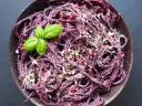 Fioletowy makaron spaghetti z buraczanym pesto, posypany orzechami i udekorowany listkiem bazylii.