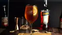 Orzeźwiający Aperol Spritz z plasterkiem pomarańczy, obok butelka Aperol. Idealny wybór zamiast Hugo.