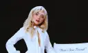 Sabrina Carpenter w białej koszuli, z rozpuszczonymi blond włosami, wygląda jak "man's best friend" na tle czerni.