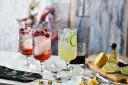 Trzy drinki z lodem i owocami: dwa czerwone z malinami, jeden żółty z limonką.