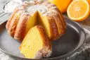 Puszysta babka na oleju, oprószona cukrem pudrem, z pomarańczami w tle. Idealna na niedzielne popołudnie.