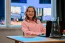 Uśmiechnięta Dorota Krempa pracuje przy laptopie, siedząc przy stole. W tle widać okno z nocnym widokiem.