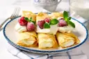 Rolowane naleśniki z mascarpone, udekorowane malinami i miętą, wyglądają apetycznie.