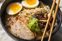 Miseczka aromatycznego ramenu z plastrami wieprzowiny, jajkiem na pół, grzybami i szczypiorkiem. Idealny ramen przepis na rozgrzewający posiłek.