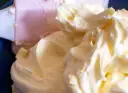 Puszysty, prosty krem z mascarpone bez śmietany, idealny do deserów. Widać go na niebieskim tle, obok różowej łopatki.