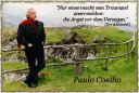 Mann mit rotem Schal und Anzug steht auf einem Hügel mit Zitat von Paulo Coelho.