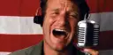Robin Williams z mikrofonem i słuchawkami na tle flagi. W jakich filmach grał Robin Williams?