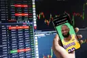 Czy giełda to hazard? Na ekranie telefonu LeBron James z pytaniem, czy idzie do kasy. Wykresy giełdowe w tle.