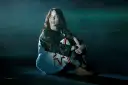 Billie Eilish siedzi na scenie, wpatrzona w dal. Jej stylizacja nawiązuje do estetyki jej albumu.