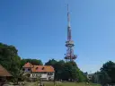 Wieża widokowa na górze Ślęża góruje nad budynkiem schroniska i zielonymi drzewami.