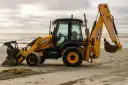 Żółta koparko-ładowarka firmy JCB stoi na piaszczystej plaży, gotowa do pracy.