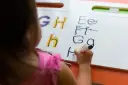Dziecko ćwiczy łączenie liter pisanych na tablicy. Litery G, H, h, E, F, G, H.