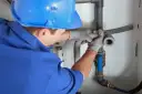 Instalator w niebieskim kasku i rękawicach montuje elementy instalacji kanalizacyjnej.