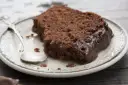 Pyszny murzynek na oleju, oblany gęstą czekoladą, czeka na talerzyku z łyżeczką.