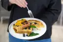 Gofry z bitą śmietaną i owocami kontra naleśniki na słodko. Widok z góry na talerz z deserem.