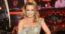 Uśmiechnięta Aleksandra Grabowska w złotej sukni z cekinami, na tle sceny "Dancing with the Stars".