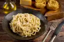 Kremowe fettuccine alfredo na czarnym talerzu, obok surowy makaron, ser i oliwa.