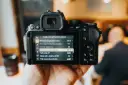 Dłoń trzyma lustrzankę cyfrową Nikon, na ekranie której widać menu nagrywania wideo z zaznaczoną opcją "Tryb ustawiania ostrości".