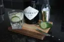 Szklanka z ginem Hendrick's i ogórkiem, obok butelka ginu, Fever-Tree i plasterki ogórka. Idealne składniki do drinków.