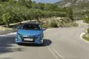 Niebieska Toyota Prius pokonuje zakręt na malowniczej drodze. Zastanawiasz się, ile pali Toyota Prius? Ten model jest znany z oszczędności.