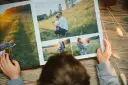Dziecko przegląda fotoksiążkę z rodzinnymi zdjęciami. W Rossmannie można wywołać zdjęcia w różnych rozmiarach, idealnych do takich albumów.