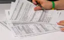 Dłoń z długopisem nad stosem dokumentów podatkowych PIT.