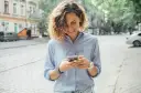 Uśmiechnięta kobieta na ulicy sprawdza telefon, być może szuka informacji o pożyczka kontomatik.