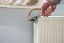 Dłoń dokręca kluczem nastawnym zawór przy grzejniku, pokazując jakie zawory do centralnego ogrzewania są potrzebne do montażu.
