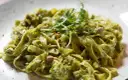 Makaron tagliatelle z zielonym sosem pesto, posypany pistacjami i udekorowany kiełkami.