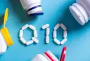 Białe tabletki ułożone w kształt "Q10" na niebieskim tle, obok otwarte pojemniki z suplementami. Koenzym Q10 na co?