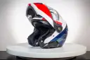 Kask motocyklowy z podniesioną szczęką, w kolorach białym, czerwonym i niebieskim, na białym tle.