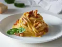 Pyszna carbonara z makaronem spaghetti, boczkiem i bazylią. W tle widać kawałek parmezanu, sugerując autentyczne carbonara skladniki.