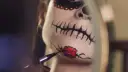 Nahaufnahme eines Gesichts mit Totenkopf-Make-up, das mit einem Pinsel bemalt wird.