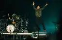 Linkin Park-Bandmitglieder auf der Bühne, ein Sänger springt, ein Schlagzeuger spielt.