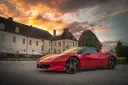 Czerwone Ferrari zaparkowane przed zabytkowym budynkiem podczas zachodu słońca.