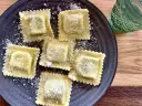 Pięć kwadratowych ravioli posypanych parmezanem na ciemnym talerzu. Idealne do domowego ravioli przepis.