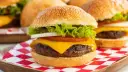 Soczysty burger z serem, sałatą, pomidorem i cebulą na czerwono-białej kratce.