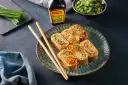 Roladki z omletu do sushi, ozdobione ikrą łososia i szczypiorkiem, obok pałeczki i sosu Maggi.